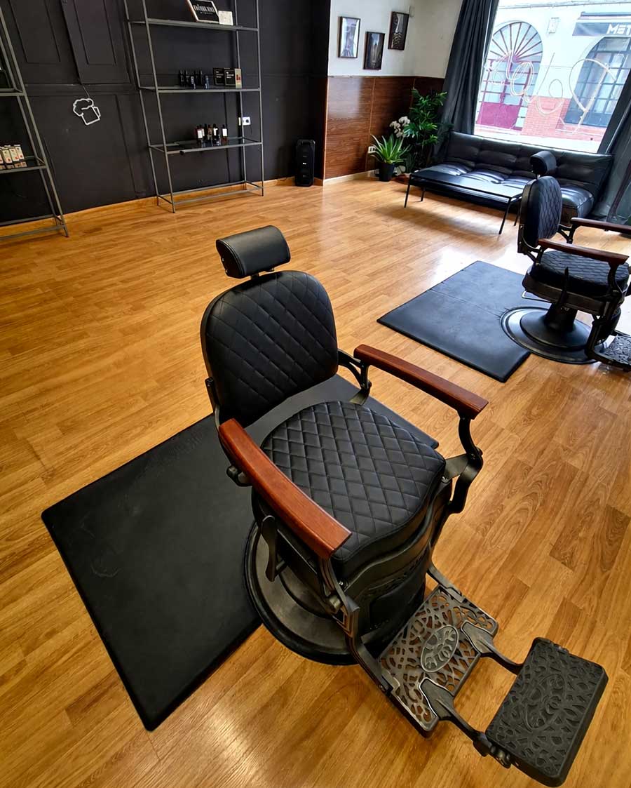 Interior de barbería moderna con sillones de corte y zona de espera.